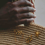 Close-up of a hand holding a woven object with gold frog-shaped charms.