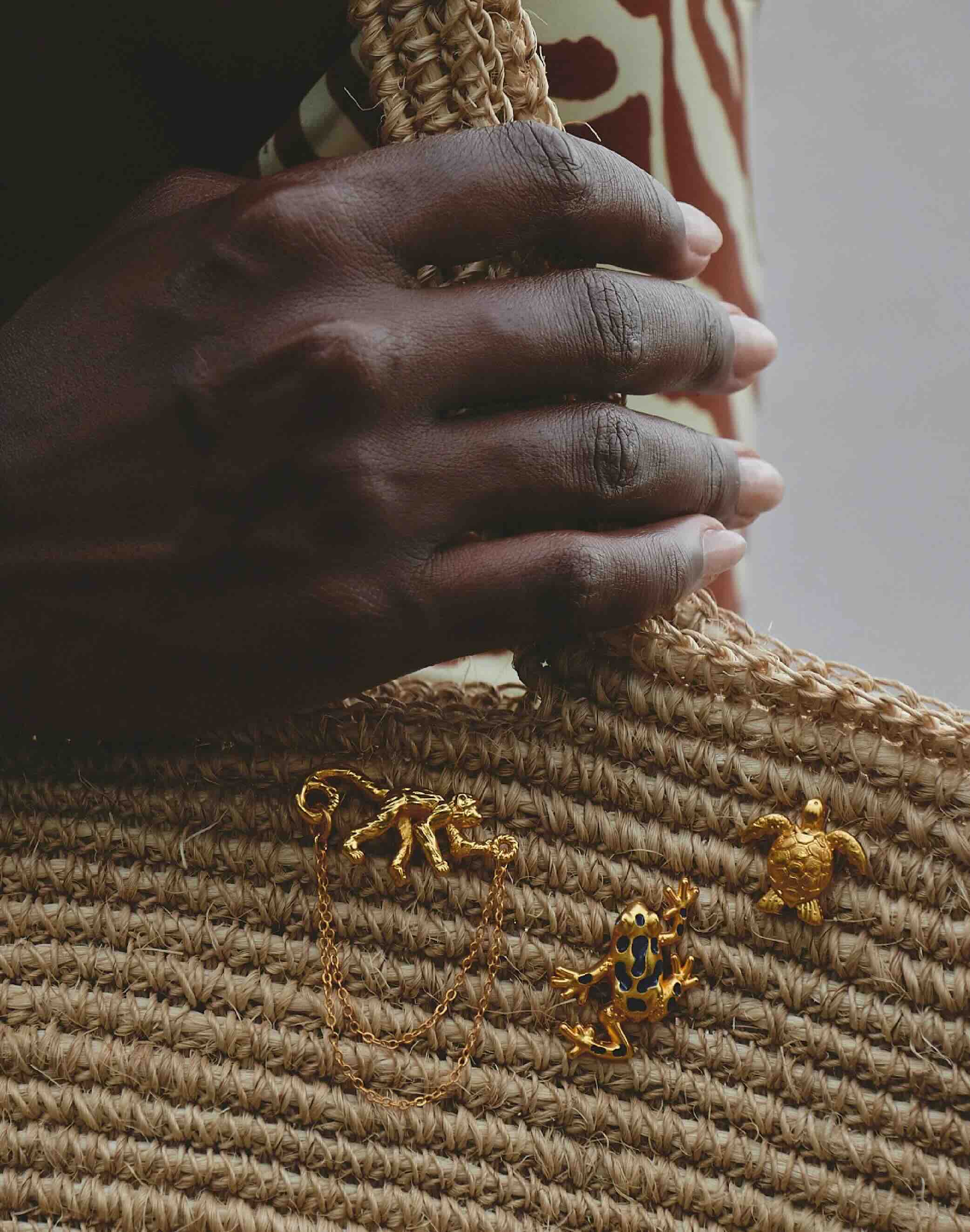 Close-up of a hand holding a woven object with gold frog-shaped charms.