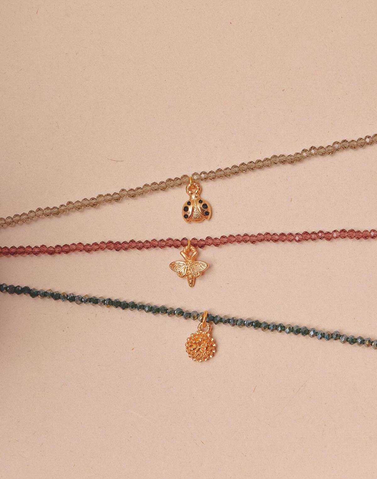 Three delicate necklaces with small charms on a beige background