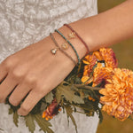 Hand wearing multiple bracelets with a bouquet of orange flowers.