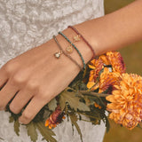 Hand wearing multiple bracelets with a bouquet of orange flowers.