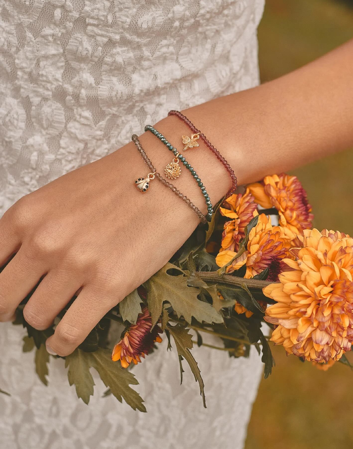 Hand wearing multiple bracelets with a bouquet of orange flowers.