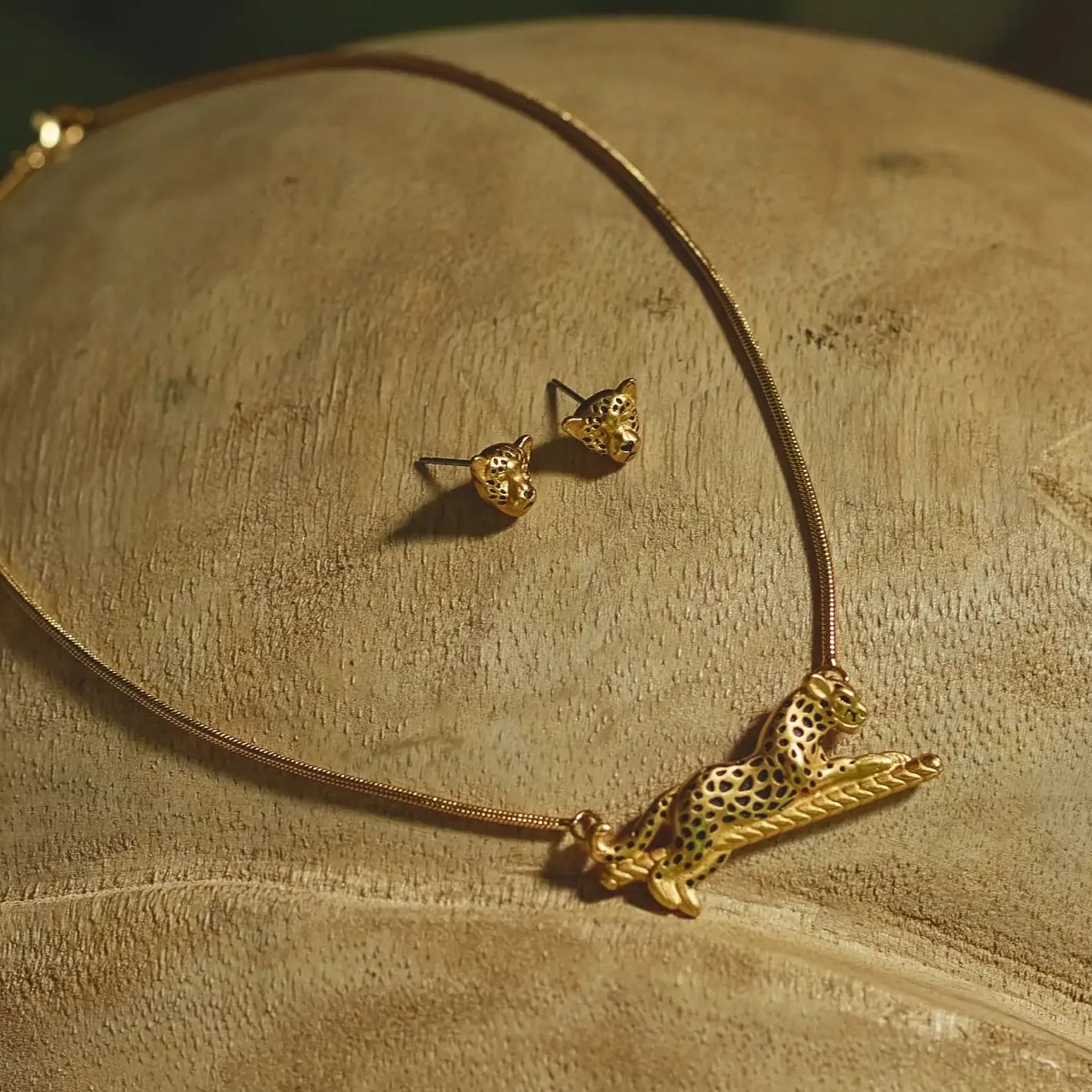 A close-up of gold-plated jaguar necklace and earrings set, placed on a wooden surface.