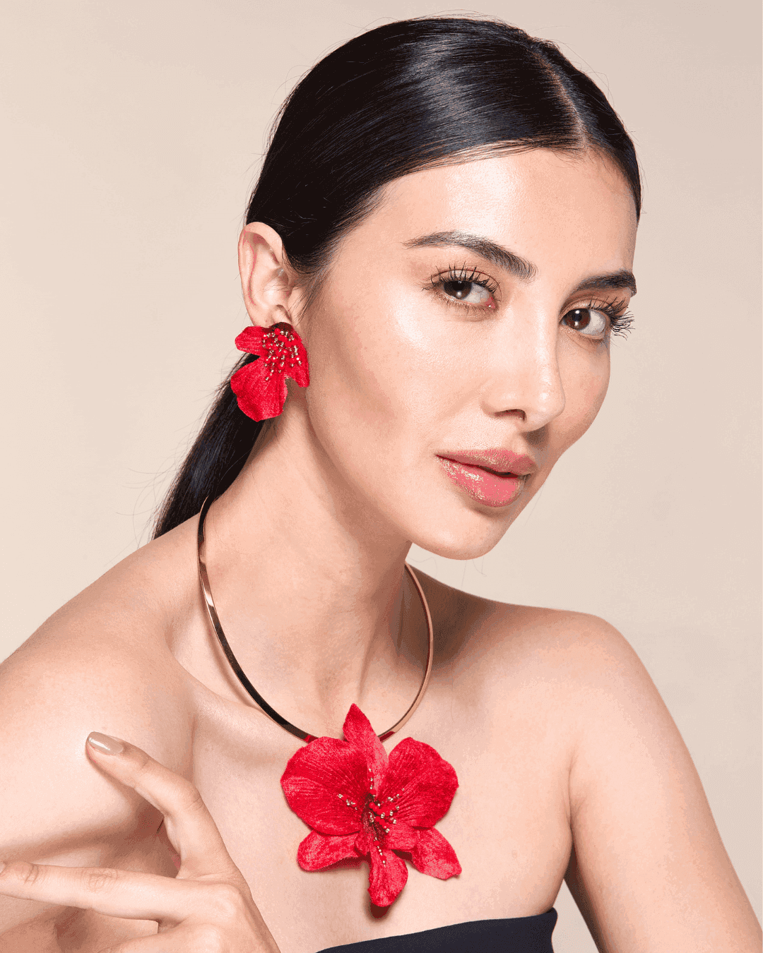 Woman wearing a red floral earring and necklace against a beige background