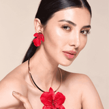 Woman wearing a red floral earring and necklace against a beige background