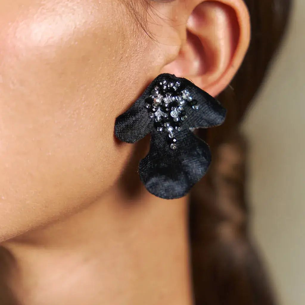 Close-up of a person wearing black floral earrings with glittery centers.