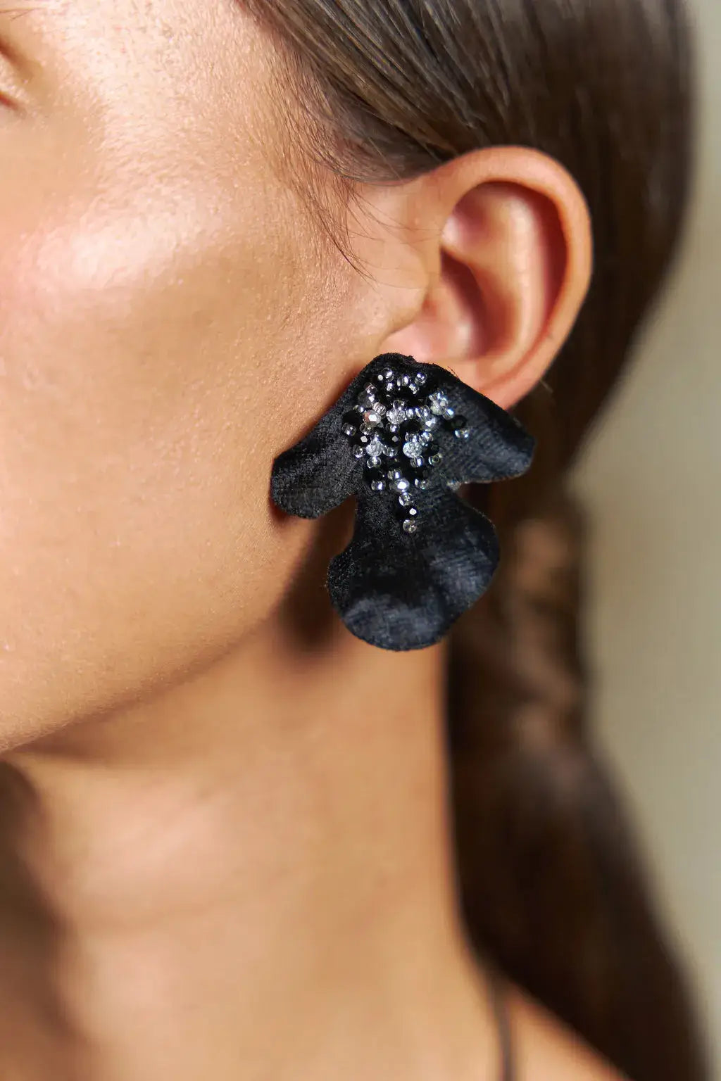 Close-up of a person wearing black floral earrings with glittery centers.