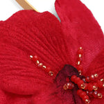 Close-up of a red knitted flower with bead embellishments on a white background