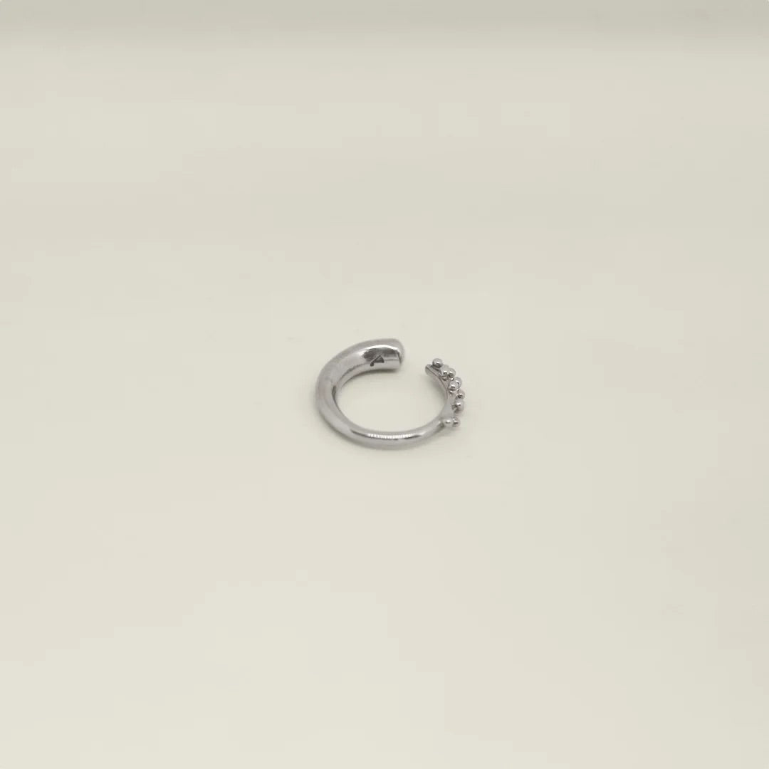 Silver hoop ring with dot detailing on a light beige background.