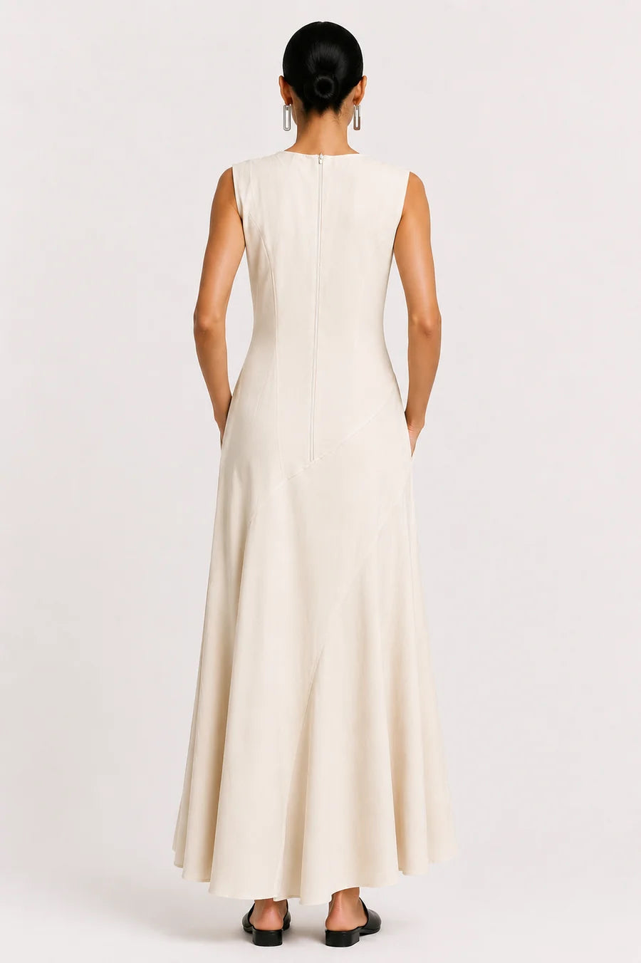 A woman viewed from the back wearing a sleeveless, floor-length cream dress with a straight neckline and a flared skirt, standing against a plain light background.