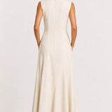 A woman viewed from the back wearing a sleeveless, floor-length cream dress with a straight neckline and a flared skirt, standing against a plain light background.