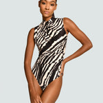 A model wearing a sleeveless high-neck one-piece swimsuit with a bold black and beige zebra print, posed against a solid light gray background.