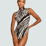 A model wearing a sleeveless high-neck one-piece swimsuit with a bold black and beige zebra print, posed against a solid light gray background.