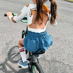 Child riding a bicycle on a paved road with grass and trees in the background