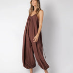 Model wearing a brown jumpsuit. She's standing behind a white background. The purpose of this image is to highlight the jumpsuit, which is available at EVAMAIA boutique in Los Angeles.