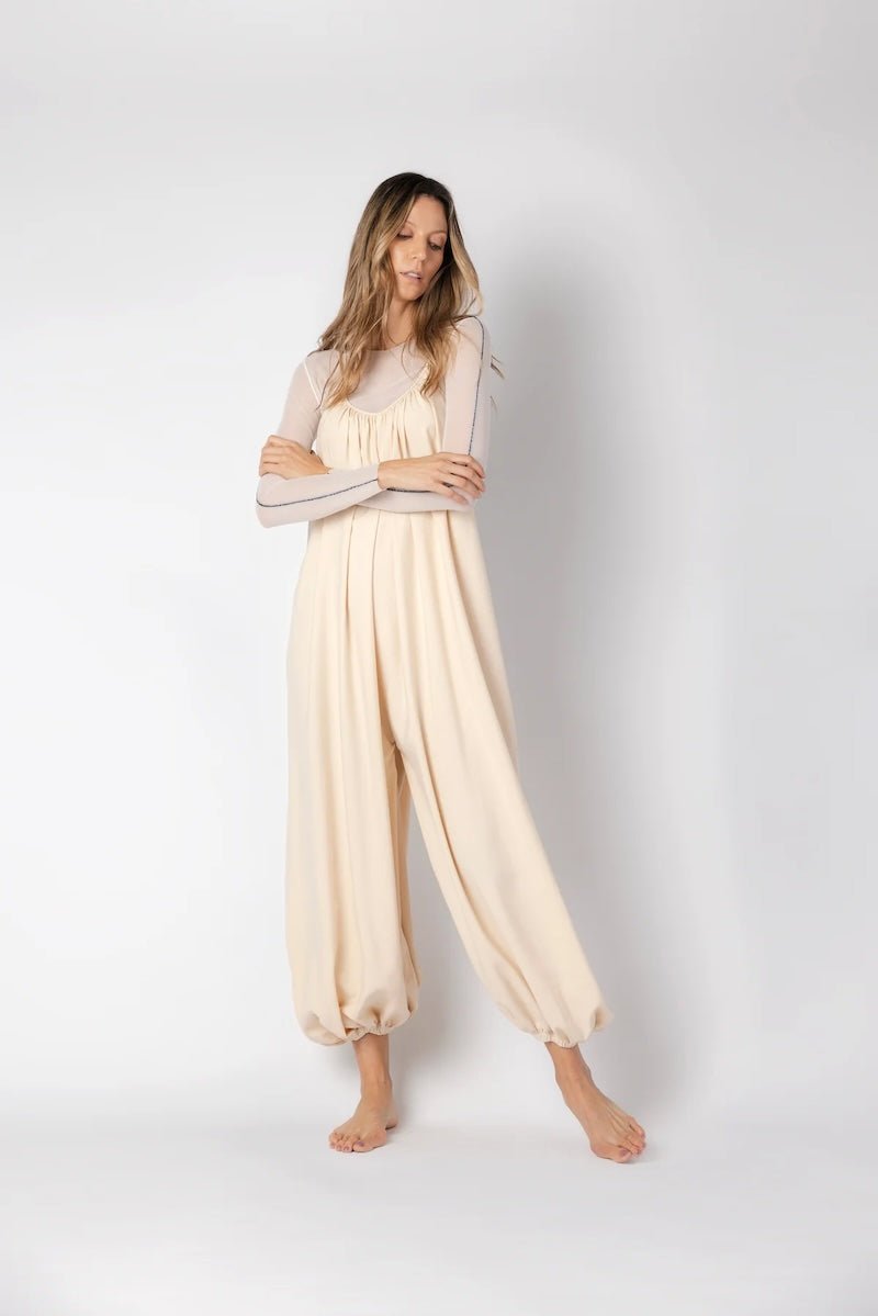 Model wearing a beige jumpsuit. She's standing behind a white background. The purpose of this image is to highlight the jumpsuit, which is available at EVAMAIA boutique in Los Angeles.