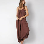 Model wearing a brown jumpsuit. She's standing behind a white background. The purpose of this image is to highlight the jumpsuit, which is available at EVAMAIA boutique in Los Angeles.