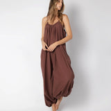 Model wearing a brown jumpsuit. She's standing behind a white background. The purpose of this image is to highlight the jumpsuit, which is available at EVAMAIA boutique in Los Angeles.