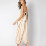 Model wearing a beige jumpsuit. She's standing behind a white background. The purpose of this image is to highlight the jumpsuit, which is available at EVAMAIA boutique in Los Angeles.