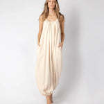 Model wearing a beige jumpsuit. She's standing behind a white background. The purpose of this image is to highlight the jumpsuit, which is available at EVAMAIA boutique in Los Angeles.