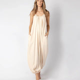 Model wearing a beige jumpsuit. She's standing behind a white background. The purpose of this image is to highlight the jumpsuit, which is available at EVAMAIA boutique in Los Angeles.