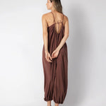 Model wearing a brown jumpsuit. She's standing behind a white background. The purpose of this image is to highlight the jumpsuit, which is available at EVAMAIA boutique in Los Angeles.