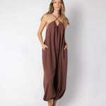 Model wearing a brown jumpsuit. She's standing behind a white background. The purpose of this image is to highlight the jumpsuit, which is available at EVAMAIA boutique in Los Angeles.