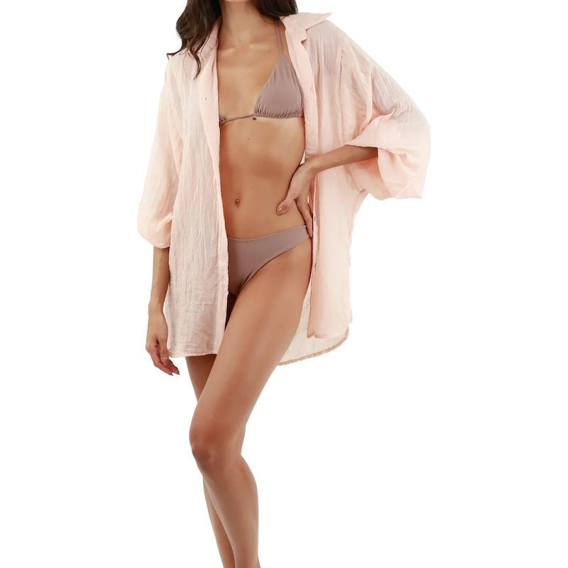 Woman wearing a light pink button down shirt over a swimsuit. She's standing against a white background. The purpose of this image is to highlight the shirt.