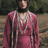 Woman in a burgundy dress with layered necklaces standing outdoors.