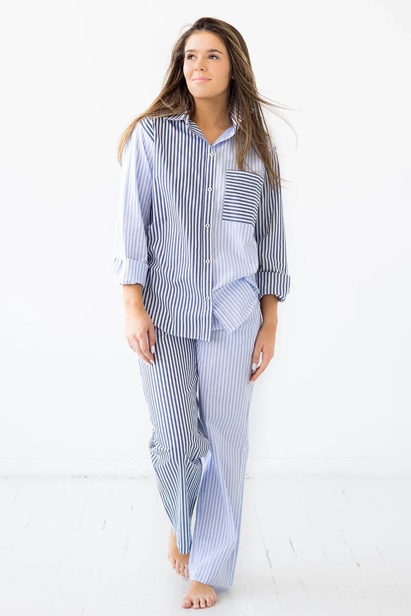 Woman wearing a long-sleeve button down shirt with blue and white stripes and matching pants. She's standing against a white background. The purpose of this image is to highlight this clothing by Salua Lingerie.