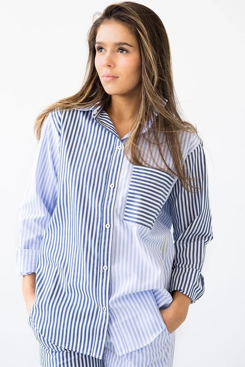 Woman wearing a long-sleeve button down shirt with blue and white stripes and matching pants. She's standing against a white background. The purpose of this image is to highlight this clothing by Salua Lingerie.