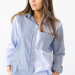 Woman wearing a long-sleeve button down shirt with blue and white stripes and matching pants. She's standing against a white background. The purpose of this image is to highlight this clothing by Salua Lingerie.