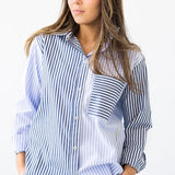 Woman wearing a long-sleeve button down shirt with blue and white stripes and matching pants. She's standing against a white background. The purpose of this image is to highlight this clothing by Salua Lingerie.