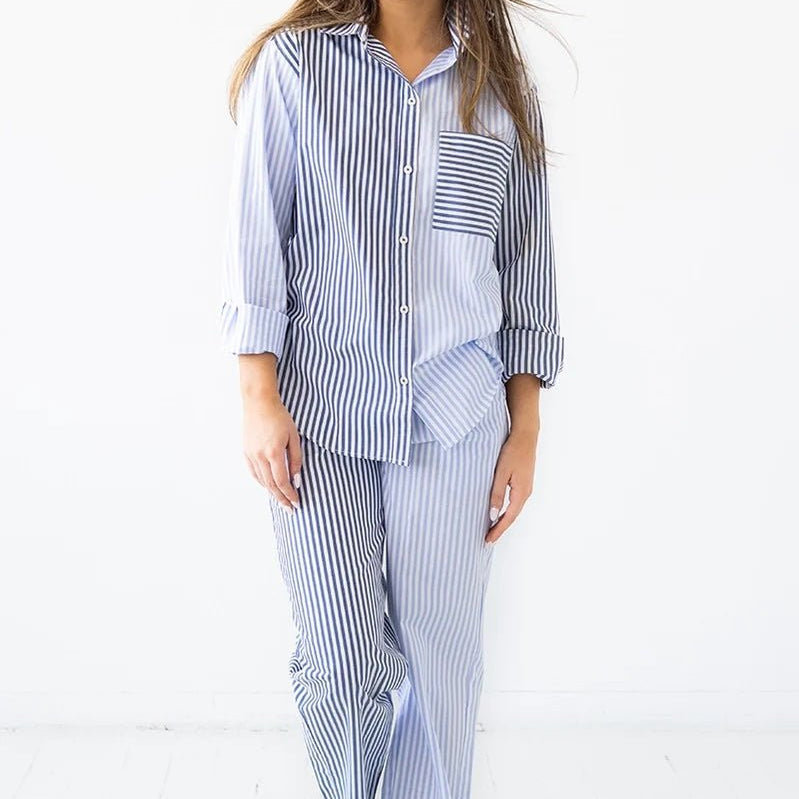Woman wearing a long-sleeve button down shirt with blue and white stripes and matching pants. She's standing against a white background. The purpose of this image is to highlight this clothing by Salua Lingerie.