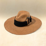 Brown wide brimmed hat with a black band and silver accent on a beige background