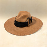 Brown wide brimmed hat with a black band and silver accent on a beige background