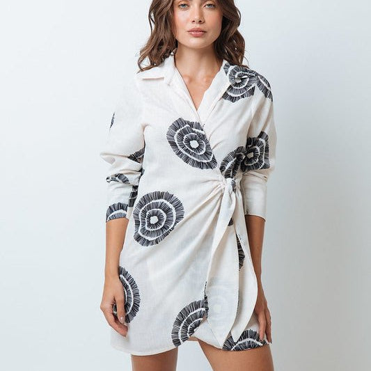 Woman wearing a black and white dress with a tie on the front. The purpose of this image is to highlight the dress because it is for sale at EVAMAIA boutique in Studio City, CA. 