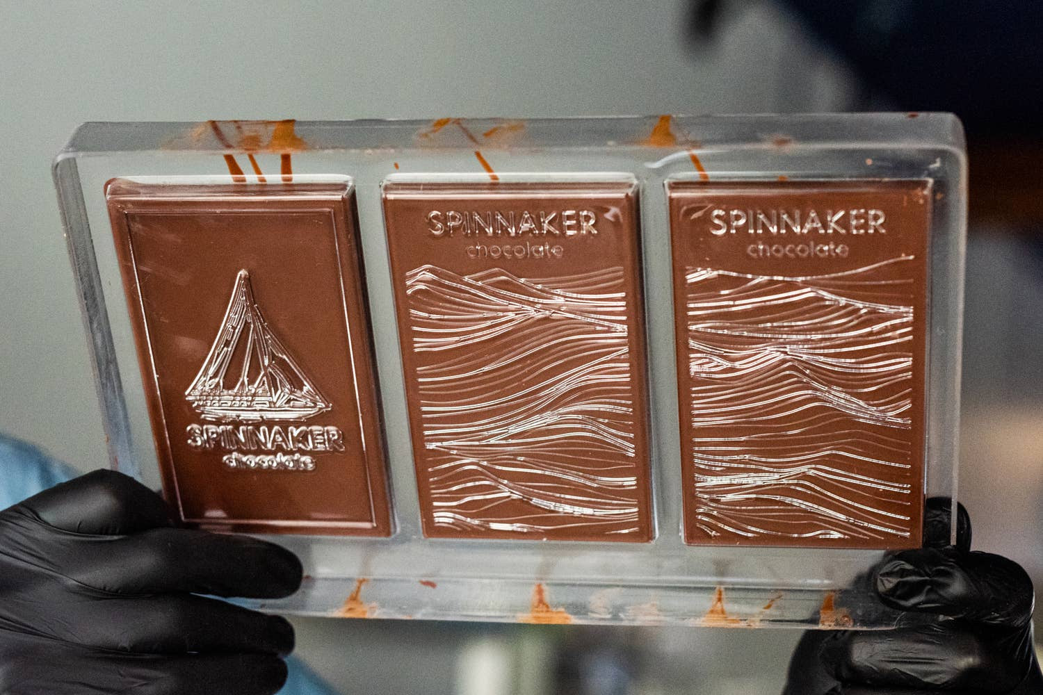 Three Spinnaker chocolate bars in a clear plastic holder with a blurred background.