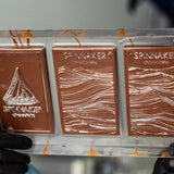 Three Spinnaker chocolate bars in a clear plastic holder with a blurred background.