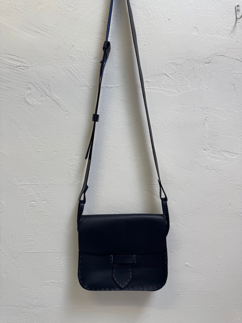 Navy blue leather crossbody bag on a light gray textured background