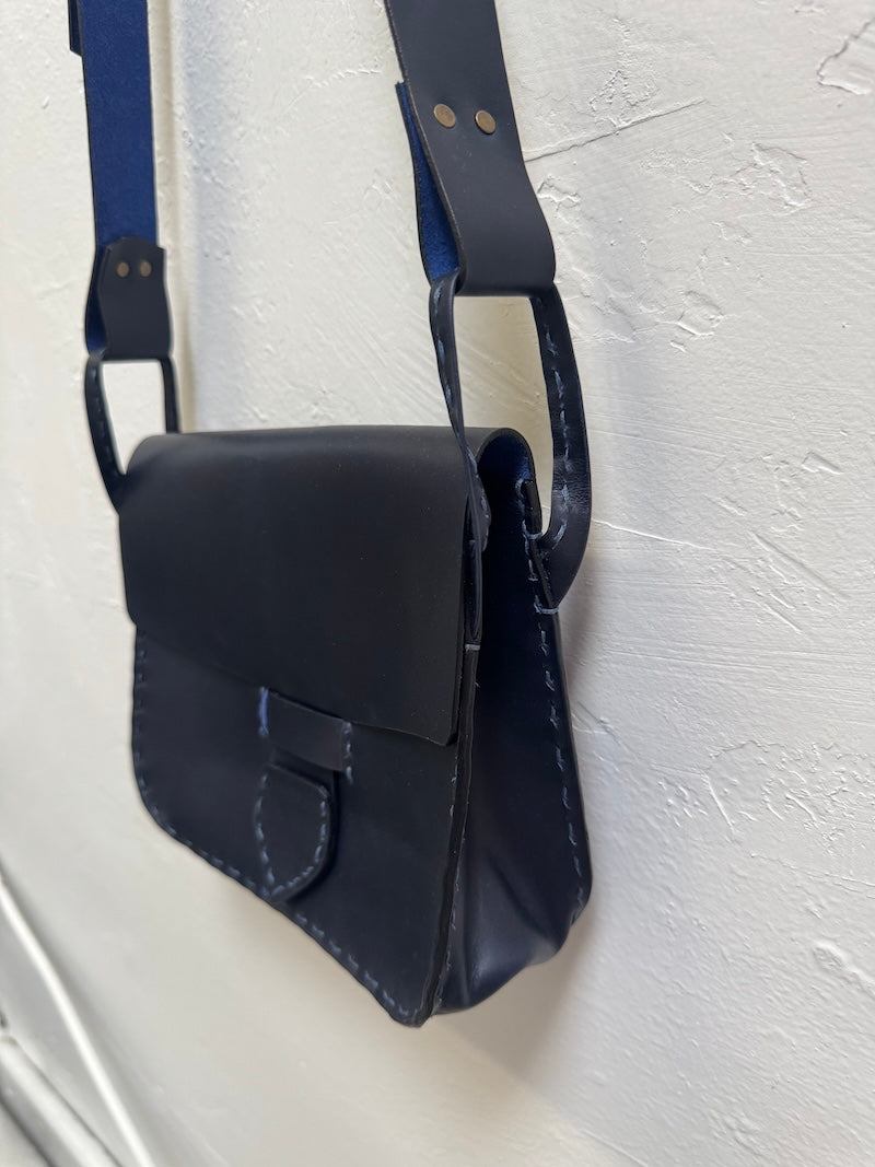 Navy blue leather bag with a strap on a light gray background