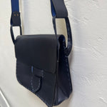 Navy blue leather bag with a strap on a light gray background