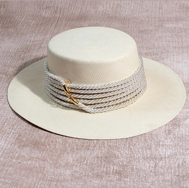 Beige straw hat with rope detail with gold accent on a textured beige background