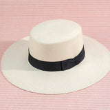 White brimmed  hat with a black band on a pink striped background