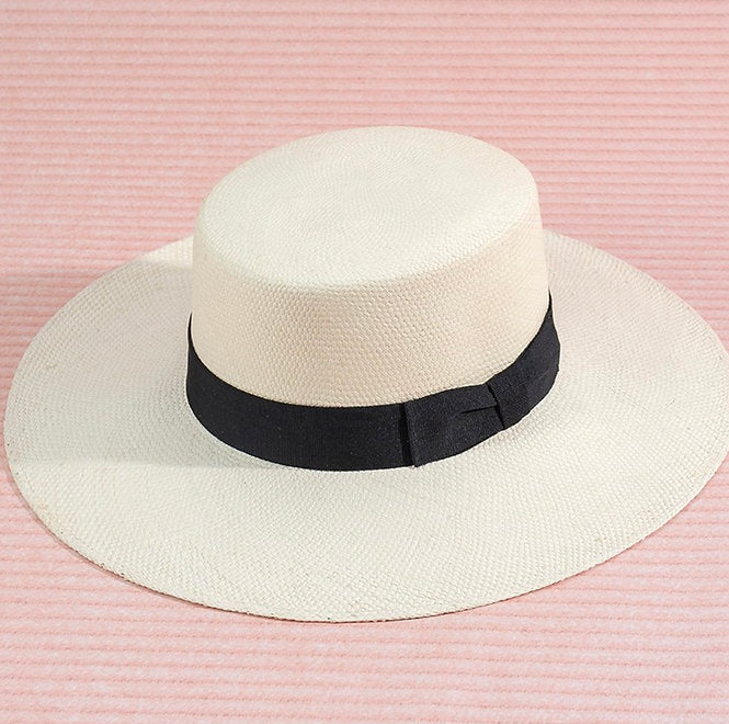 White brimmed  hat with a black band on a pink striped background