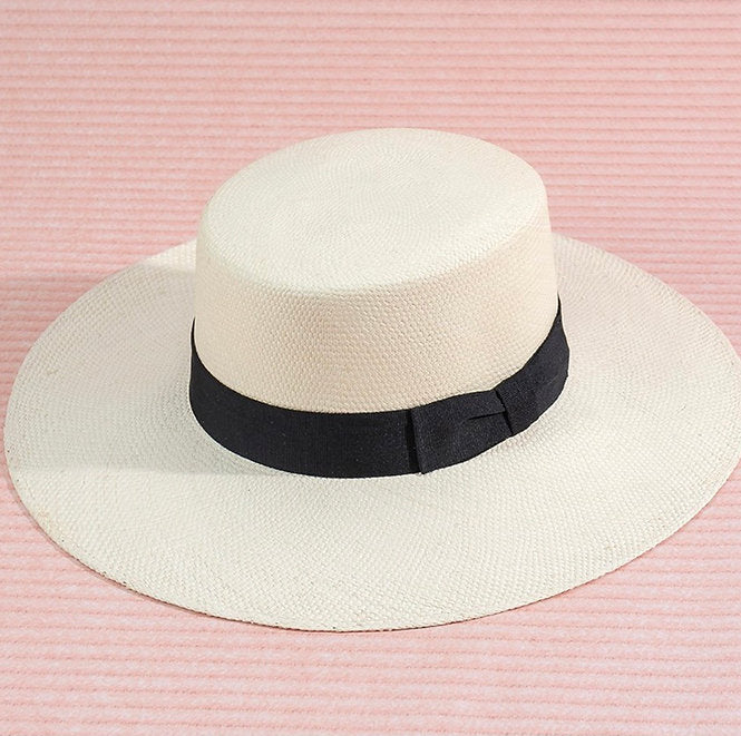 White brimmed  hat with a black band on a pink striped background