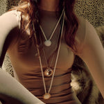 Close up image of a woman wearing 3 necklaces. Two with cords and one with a silver chain. They have the Sun and Moon. The purpose of this image is to highlight the necklaces by Pajarolimon jewelry because they are for sale at EVAMAIA Boutique in Studio City, CA.