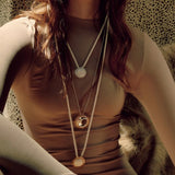Close up image of a woman wearing 3 necklaces. Two with cords and one with a silver chain. They have the Sun and Moon. The purpose of this image is to highlight the necklaces by Pajarolimon jewelry because they are for sale at EVAMAIA Boutique in Studio City, CA.