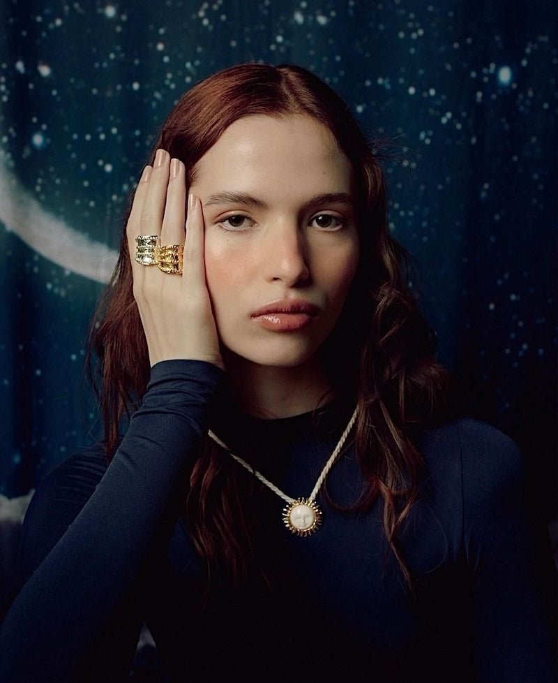 Image of a woman wearing a necklace with the sun on it and two oversized rings. The purpose of this image is to highlight the Pajarolimon jewelry because it is for sale at EVAMAIA Boutique in Studio City, CA.
