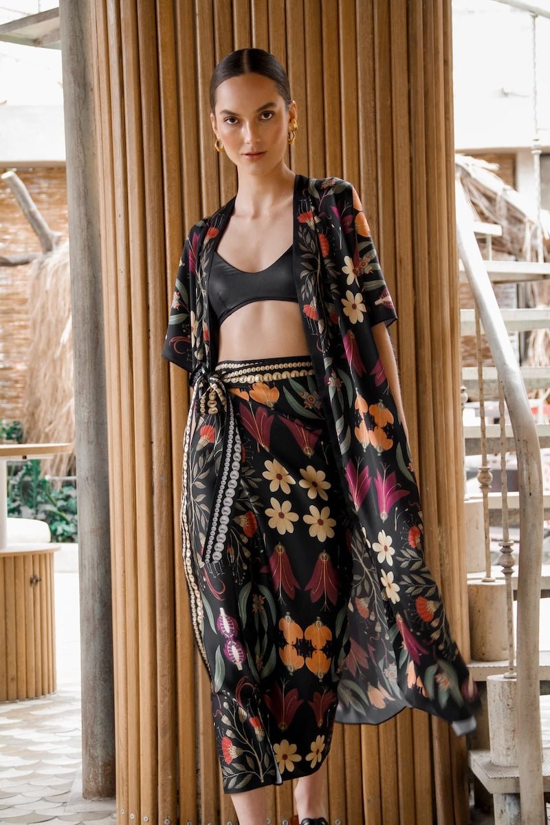 Image of a woman wearing a black skirt and matching kimono with bright flowers. The purpose of this image is to highlight the skirt, which is for sale at EVAMAIA boutique in Studio City, CA.